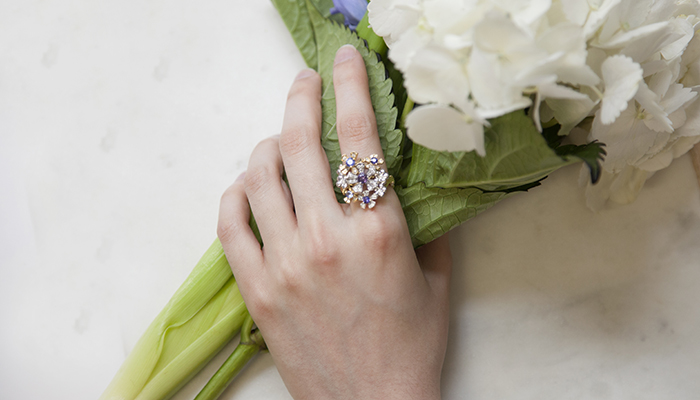 Woman's hand holding white flowers with floral-inspired ring with diamonds, purple, and blue gemstones