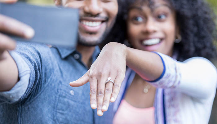 Excited newly engaged couple take selfie. They are showing off the woman's new diamond engagement ring.